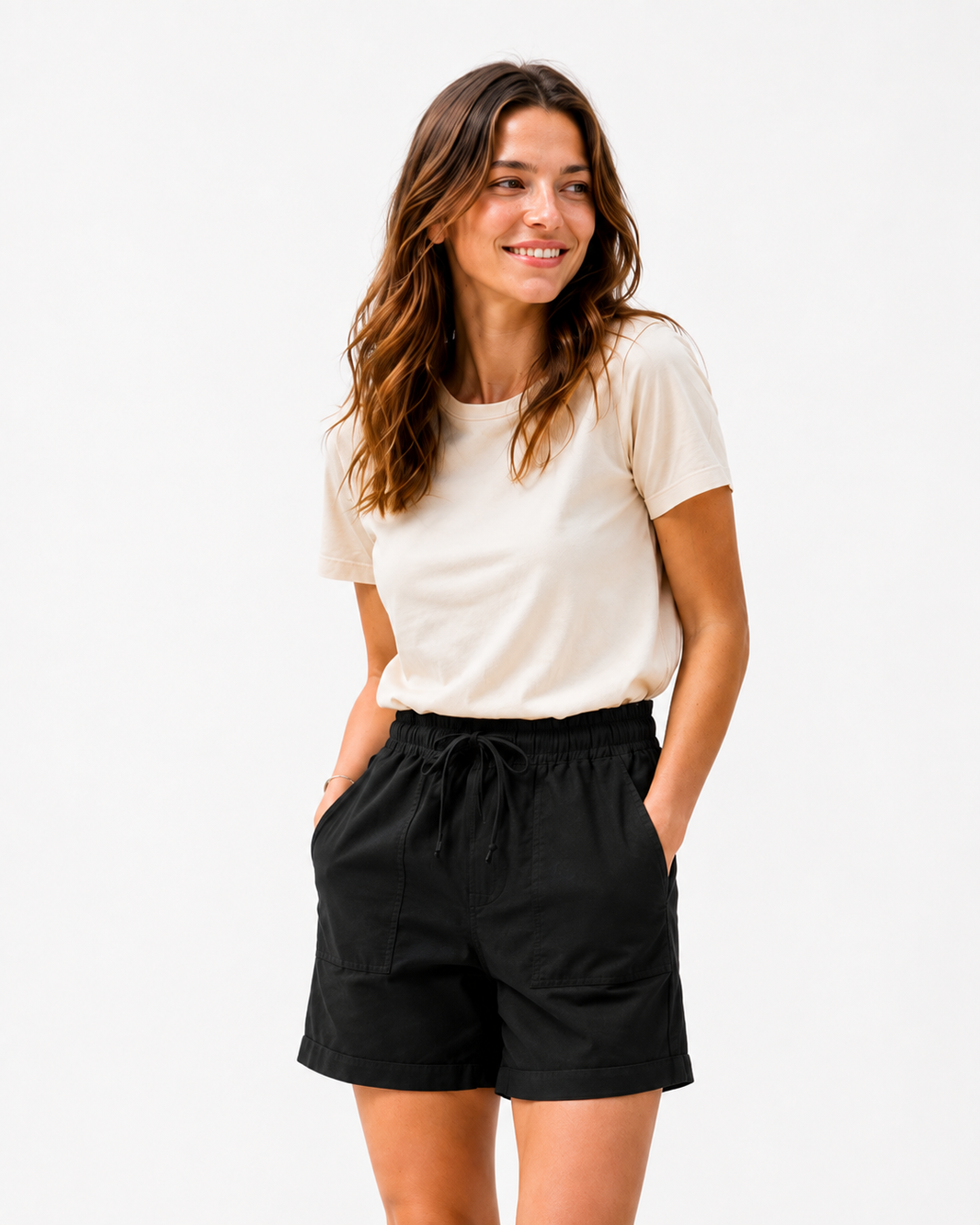 A woman modeling a cream short-sleeve t-shirt and black drawstring shorts against a plain white studio background.