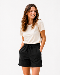 A woman modeling a cream short-sleeve t-shirt and black drawstring shorts against a plain white studio background.